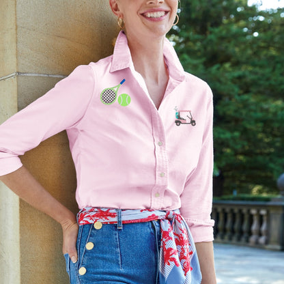 Woman wearing a pink shirt with embroidered designs, standing outdoors.