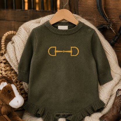 An olive green baby romper with a gold embroidered horse bit graphic on the chest, hanging on a wooden hanger over a beige knit blanket with rustic props.